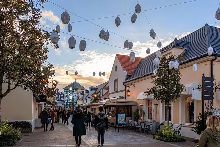 Charming pedestrian shopping street at Vallée Village outlet with decorative hanging lanterns at dusk