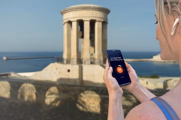 Tourist using audio guide app on smartphone at Siege Bell War Memorial in Valletta, Malta