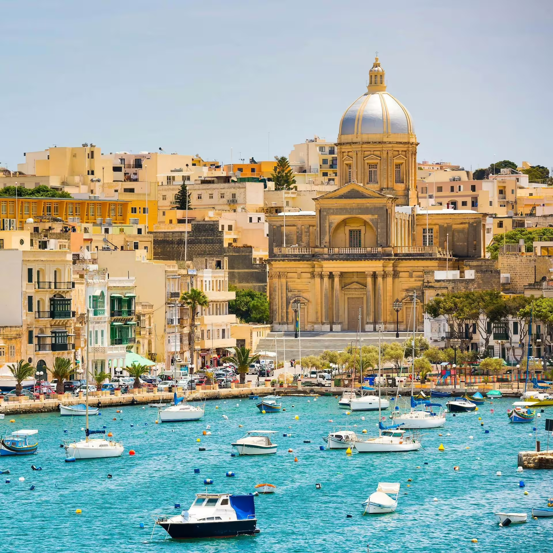 Picturesque view of the Basilica of Our Lady of Mount Carmel and vibrant waterfront with boats on a Valletta Harbours Cruise.