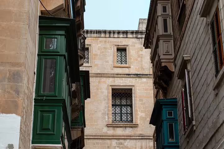 Narrow alley in Valletta with traditional green wooden balconies and limestone buildings