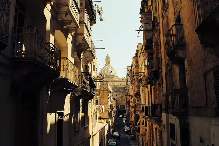 Narrow Valletta street with ornate balconies and church dome visible at the end