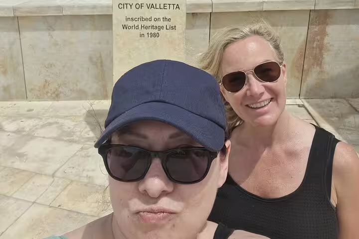 Two women smiling in front of City of Valletta UNESCO World Heritage plaque, Malta