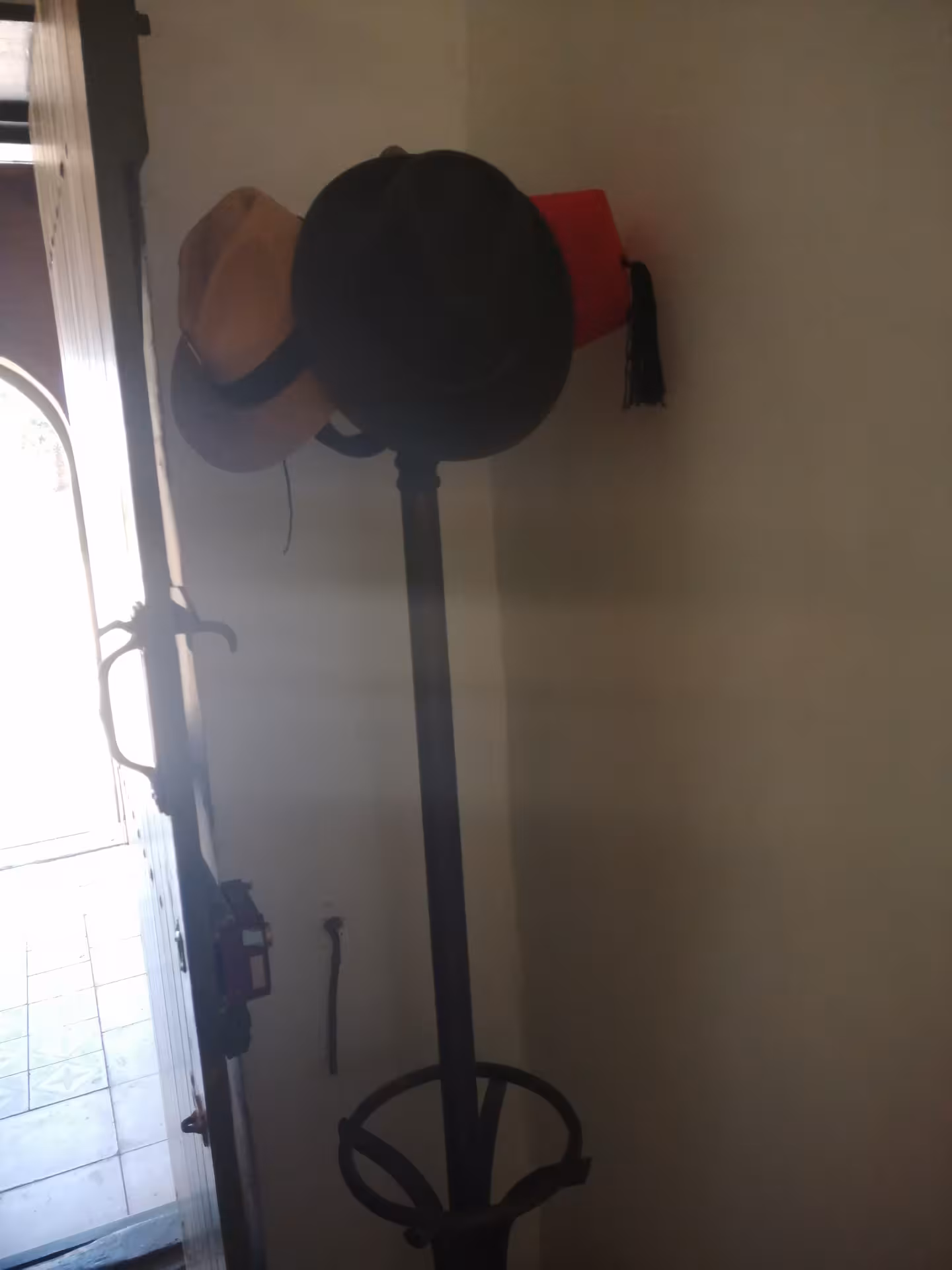 Hat stand with black bowler hat, tan fedora, and red fez with tassel near entrance door