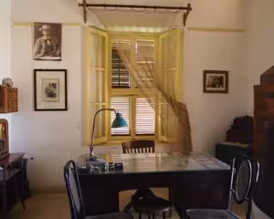 Vintage study room with yellow curtained window, desk, and framed wall portraits