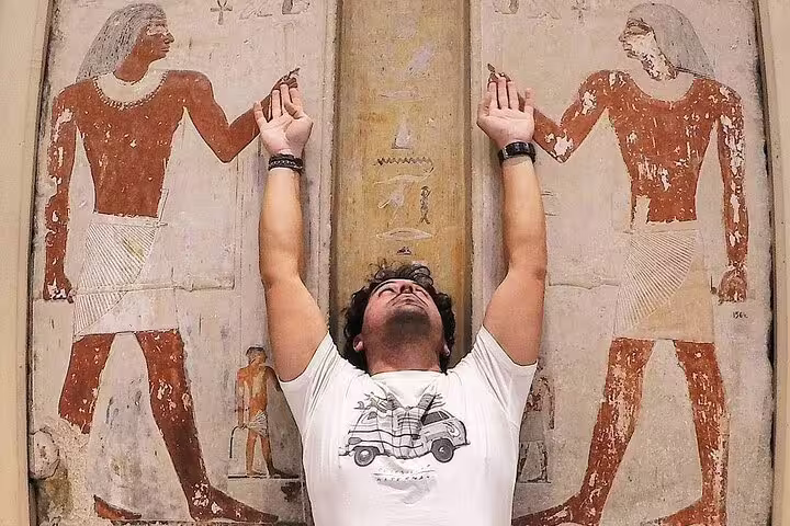 Visitor posing by ancient tomb wall paintings at Valley of the Nobles, West Bank Nile tour in Luxor Egypt