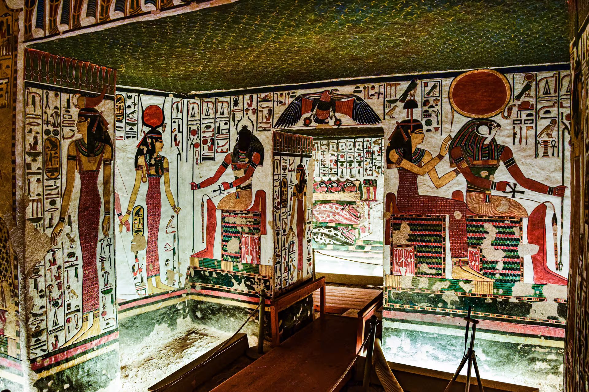 Colorful ancient Egyptian hieroglyphics and deity murals covering the walls of a Valley of the Kings tomb chamber