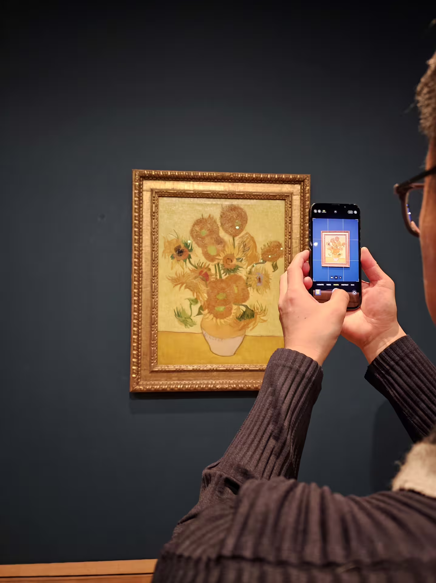Visitor photographing Van Gogh's Sunflowers painting during immersive guided tour at art museum exhibition.