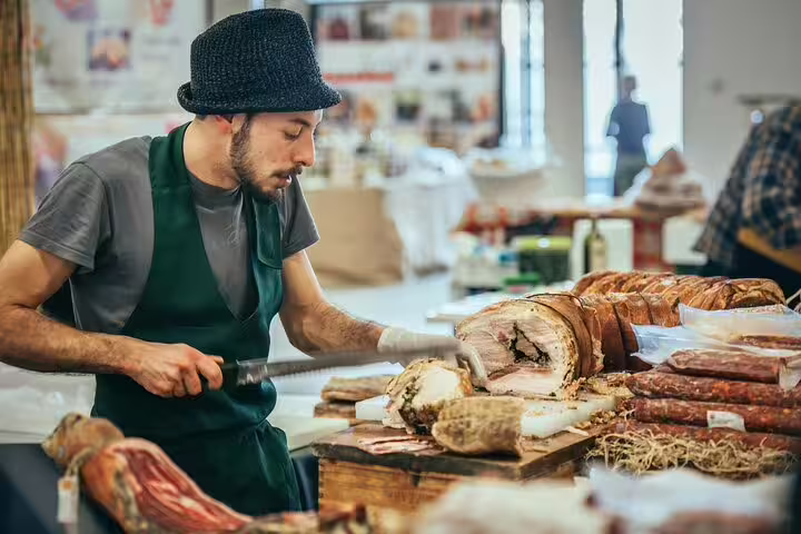 Man slicing cured meats at a vibrant Italian market, showcasing authentic culinary experiences in the Vatican Market tour.