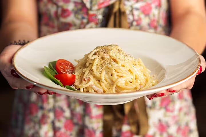 Person holding a plate of creamy spaghetti carbonara garnished with fresh basil and cherry tomatoes, perfect for Vatican Market culinary tour.