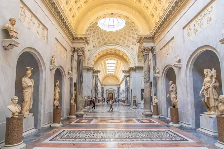 Grand marble gallery hall of Vatican Museums with classical statues in arched niches and ornate ceiling