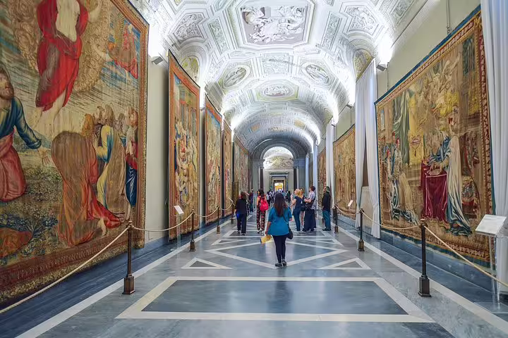 Visitors walk through the ornate tapestry gallery of the Vatican Museums on an exclusive Sistine Chapel fast track group tour