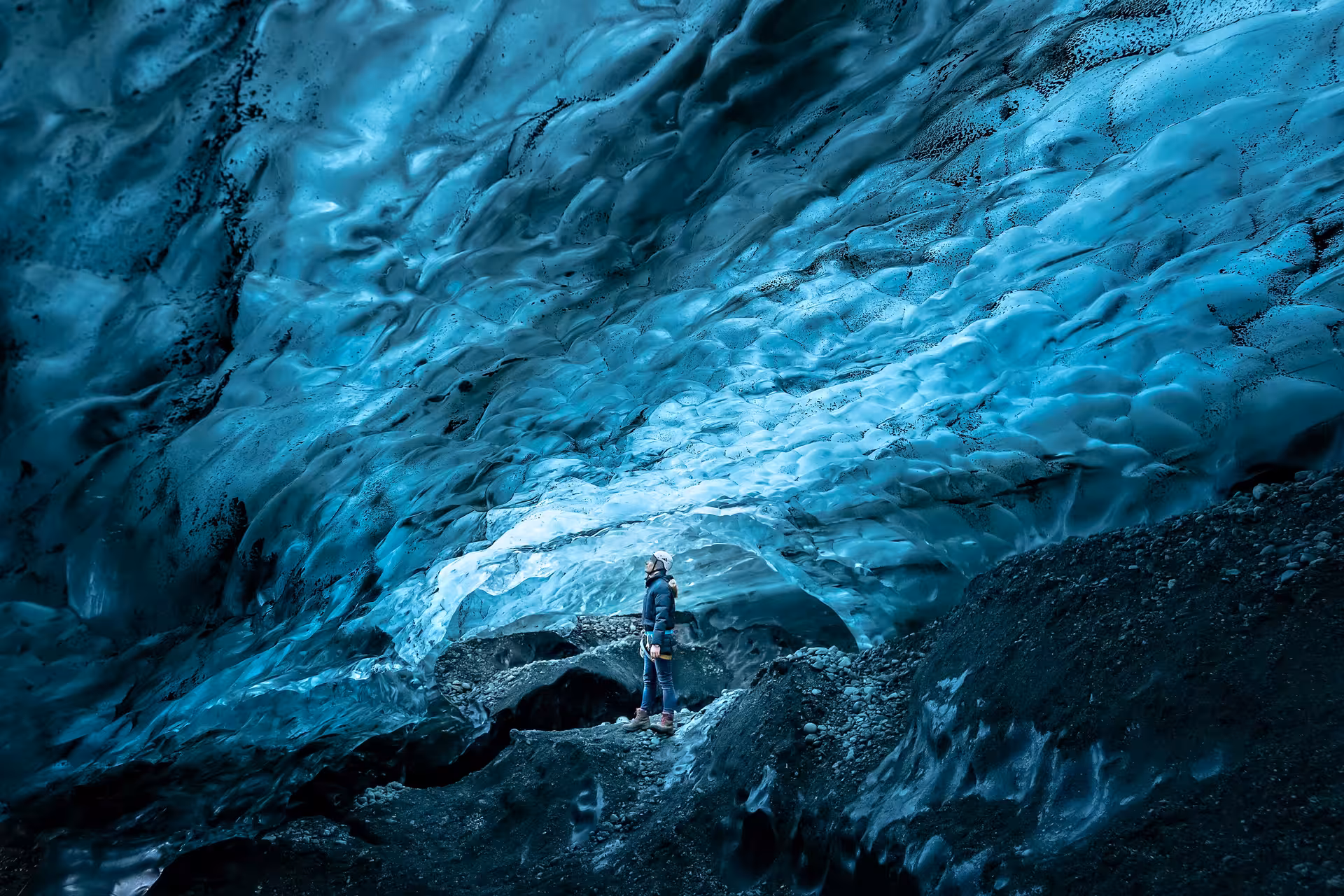 Person gazing up at glowing blue ice cave ceiling inside Vatnajokull glacier, Iceland