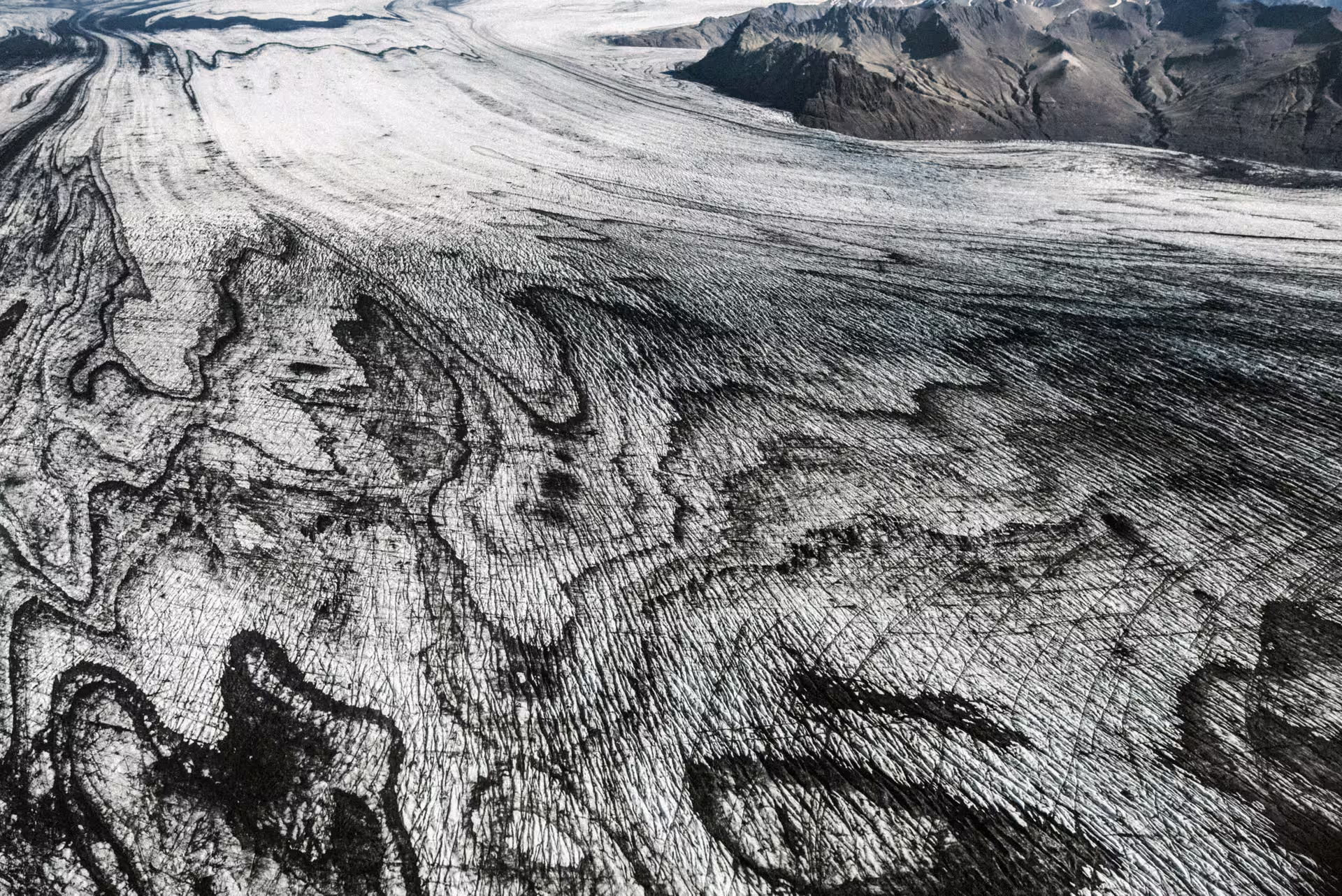 Aerial view of Vatnajokull glacier surface with dark moraine lines and rocky mountains in Iceland