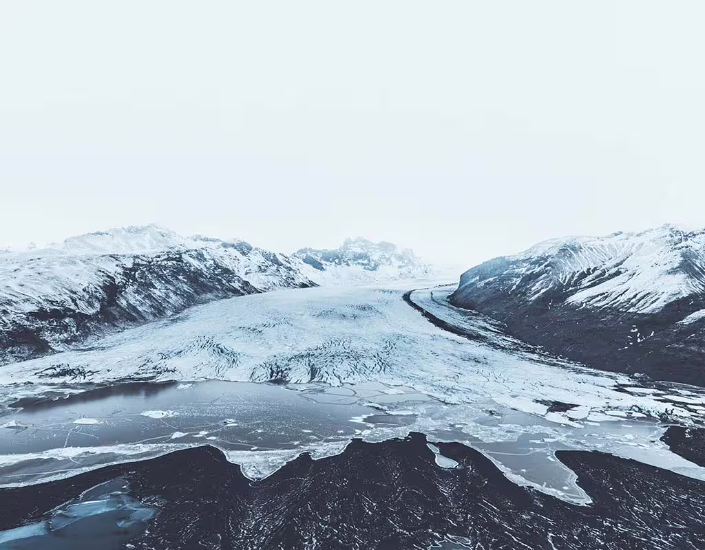 Aerial view of Vatnajokull glacier tongue flowing between snow-capped mountains into a frozen glacial lagoon
