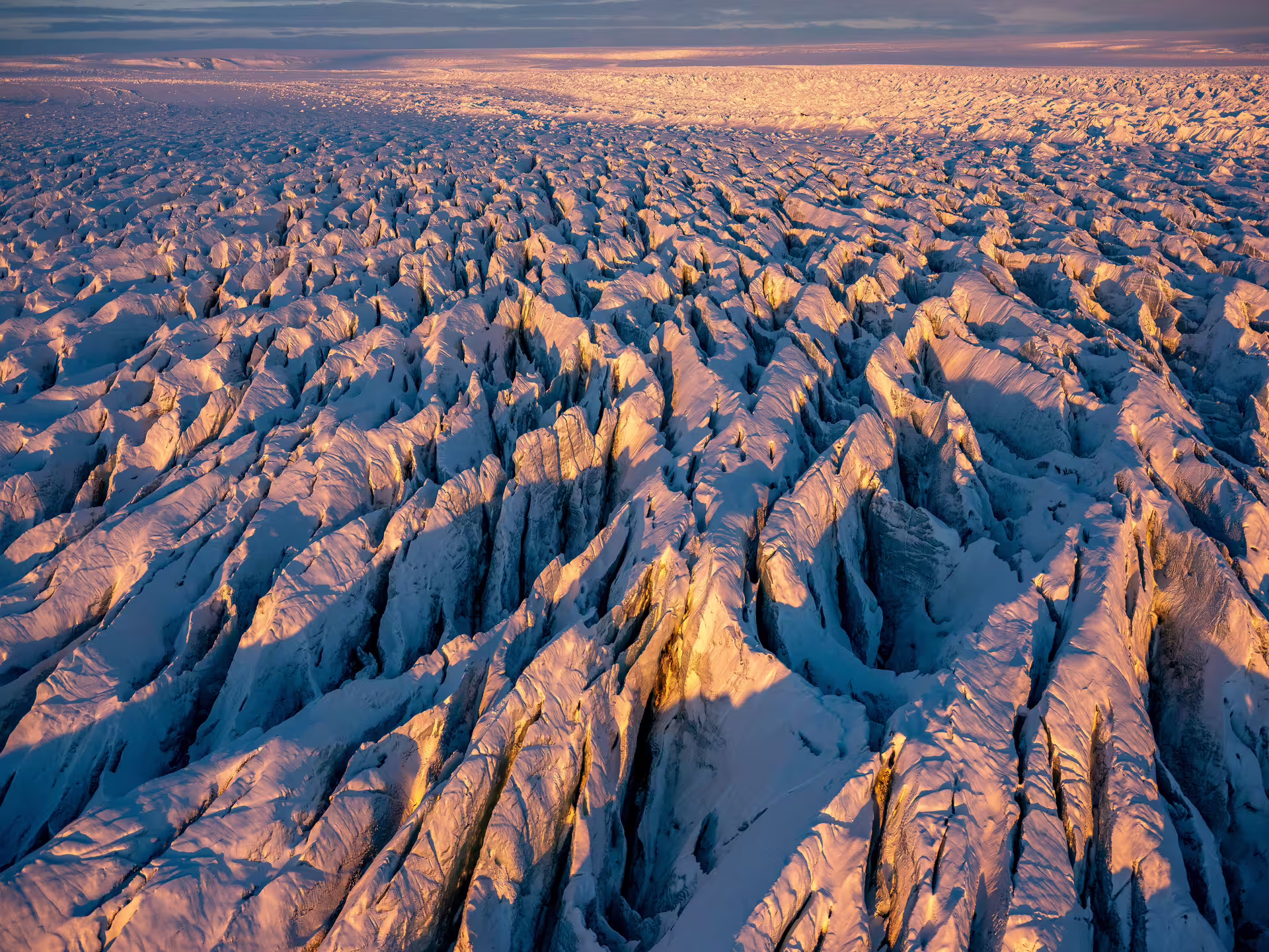Aerial view of vast glacial crevasses on Vatnajokull ice cap bathed in golden sunset light