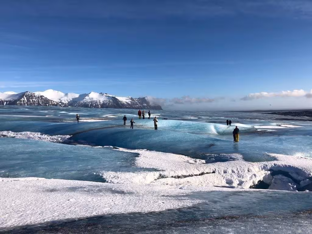 Tourists exploring the vast blue ice surface of Vatnajokull glacier in Iceland with snow-capped mountains behind