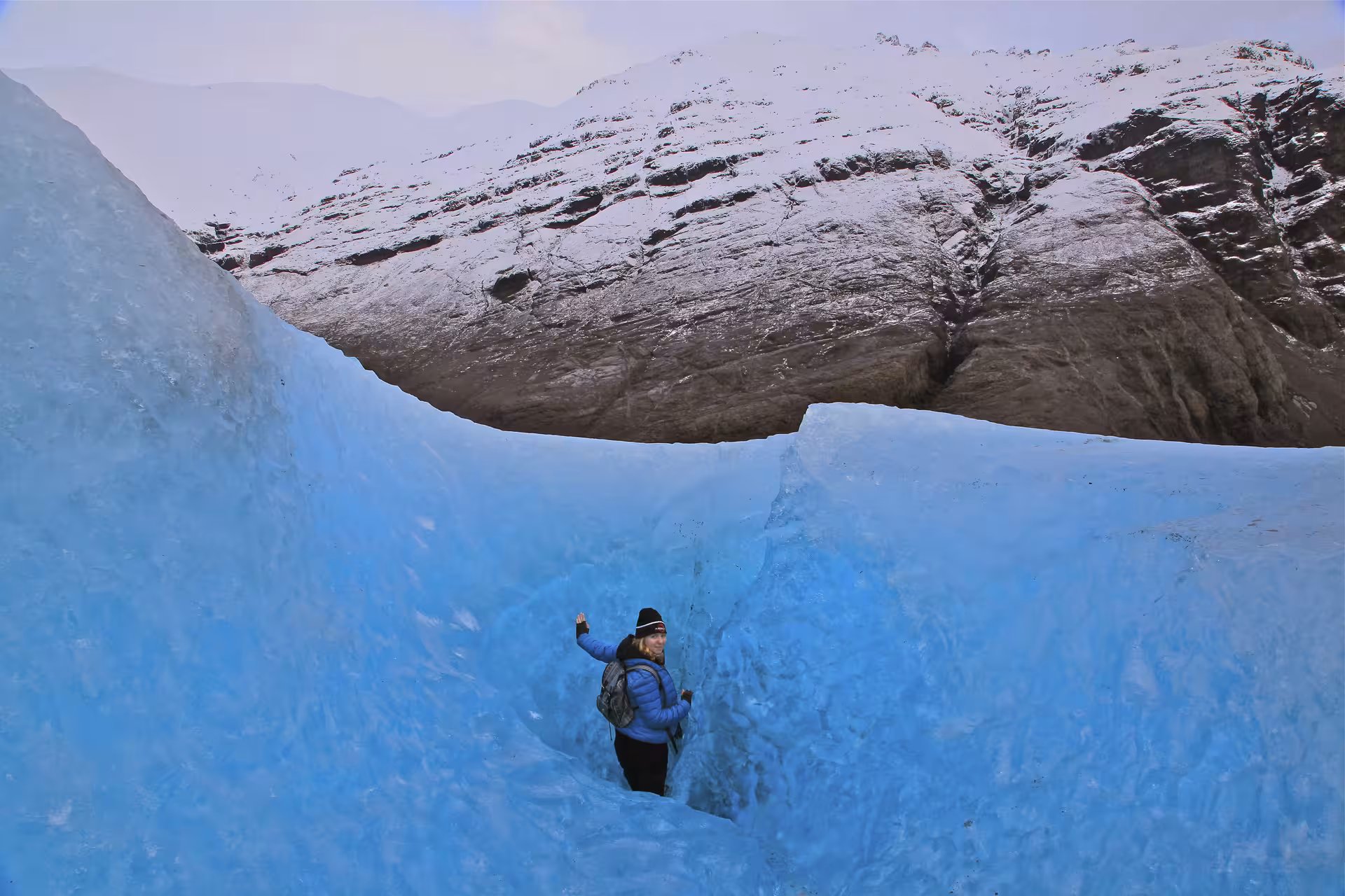 Tourist standing in blue ice crevasse on Vatnajokull Glacier Iceland with snow-covered mountains behind