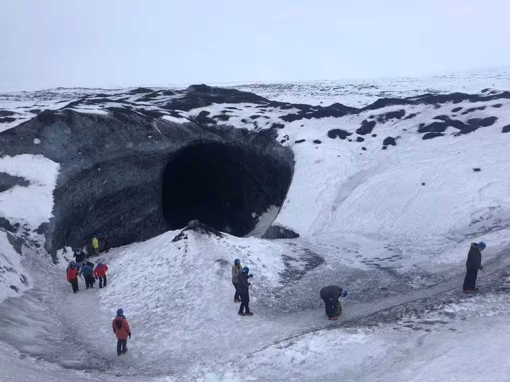 Tourists in winter gear approaching dark entrance of Vatnajokull glacier ice cave in Iceland