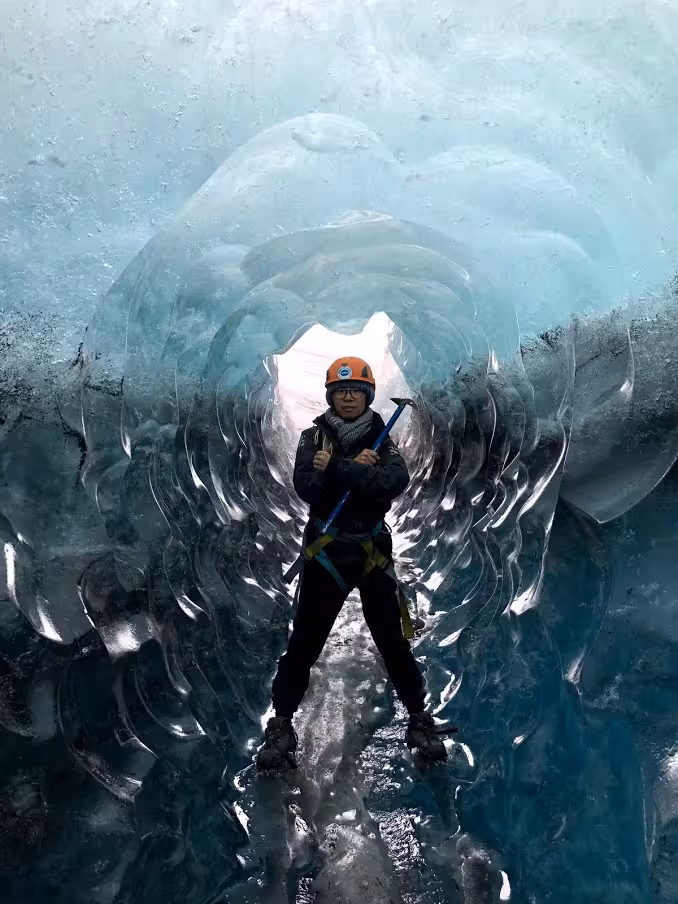 Explorer in orange helmet holding ice axe inside Vatnajokull glacier ice cave tunnel, Iceland