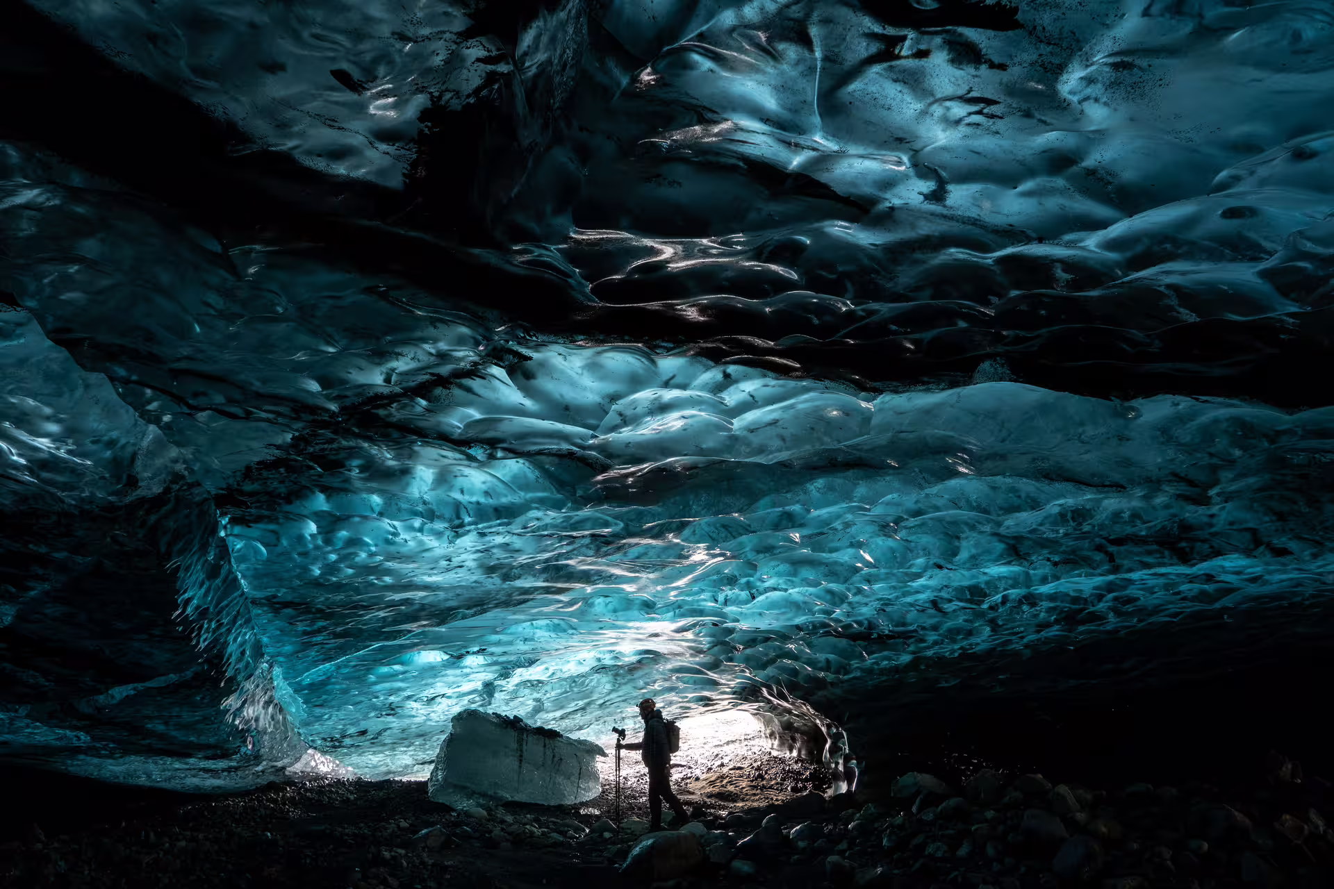 Photographer silhouetted inside a glowing blue ice cave beneath Vatnajokull glacier in Iceland