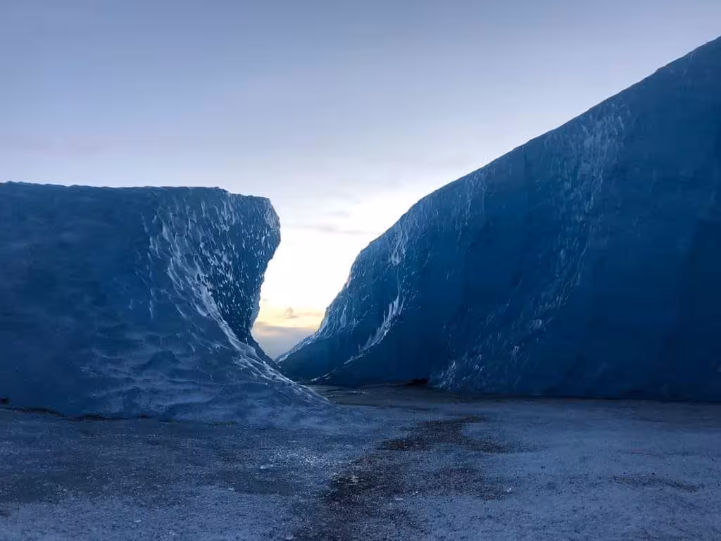 Blue glacial ice walls forming a narrow passage on Vatnajokull glacier with sunset sky visible between them