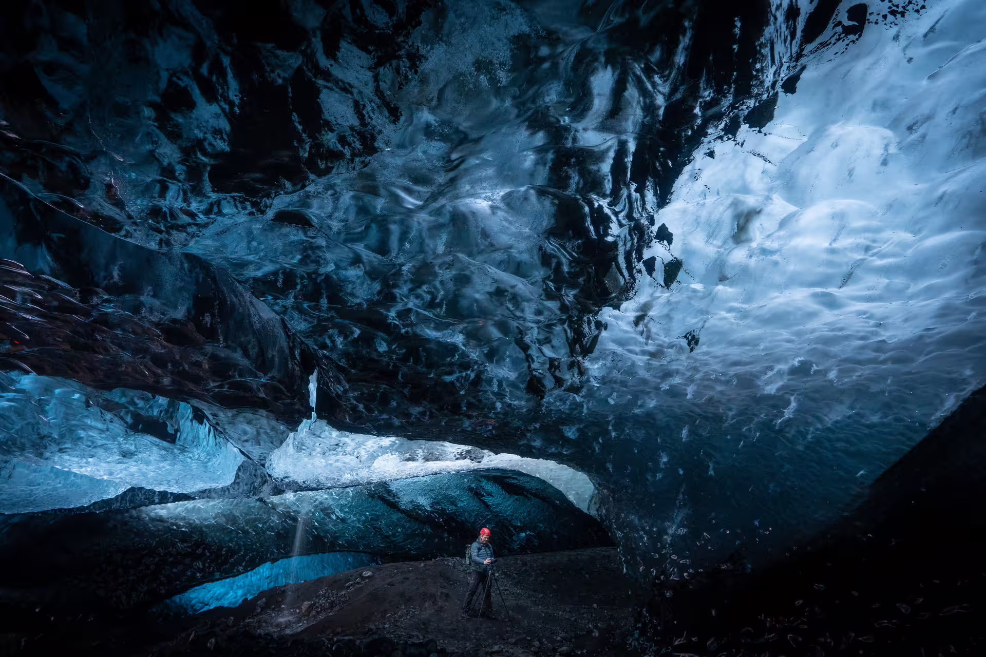 Photographer with tripod inside a massive blue glacial ice cave at Vatnajokull Iceland