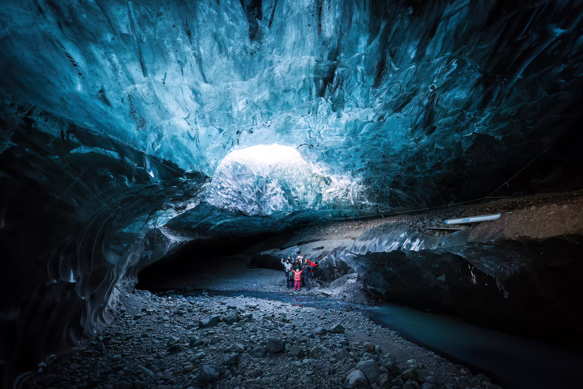 A small group of tourists exploring a stunning Iceland glacial ice cave with glowing blue crystal ice formations on a private photography tour.