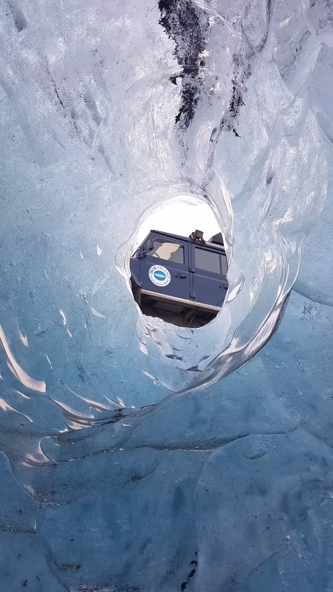 View from inside Vatnajokull glacier ice cave tunnel with Blue Iceland super jeep visible through opening