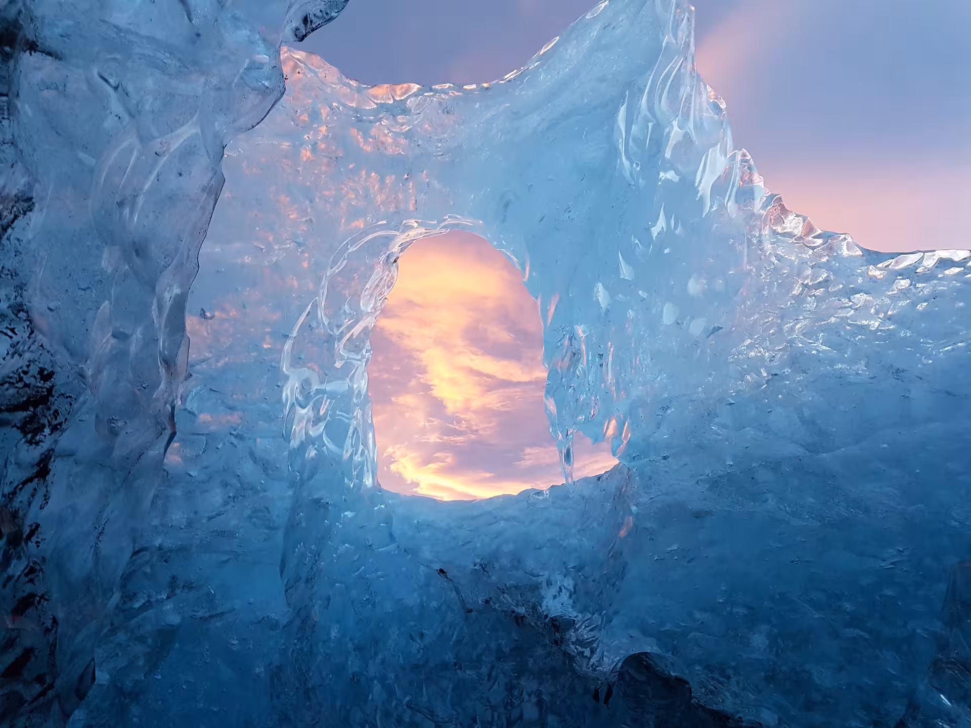 View through a natural ice tunnel in Vatnajokull glacier revealing a colorful sunset sky
