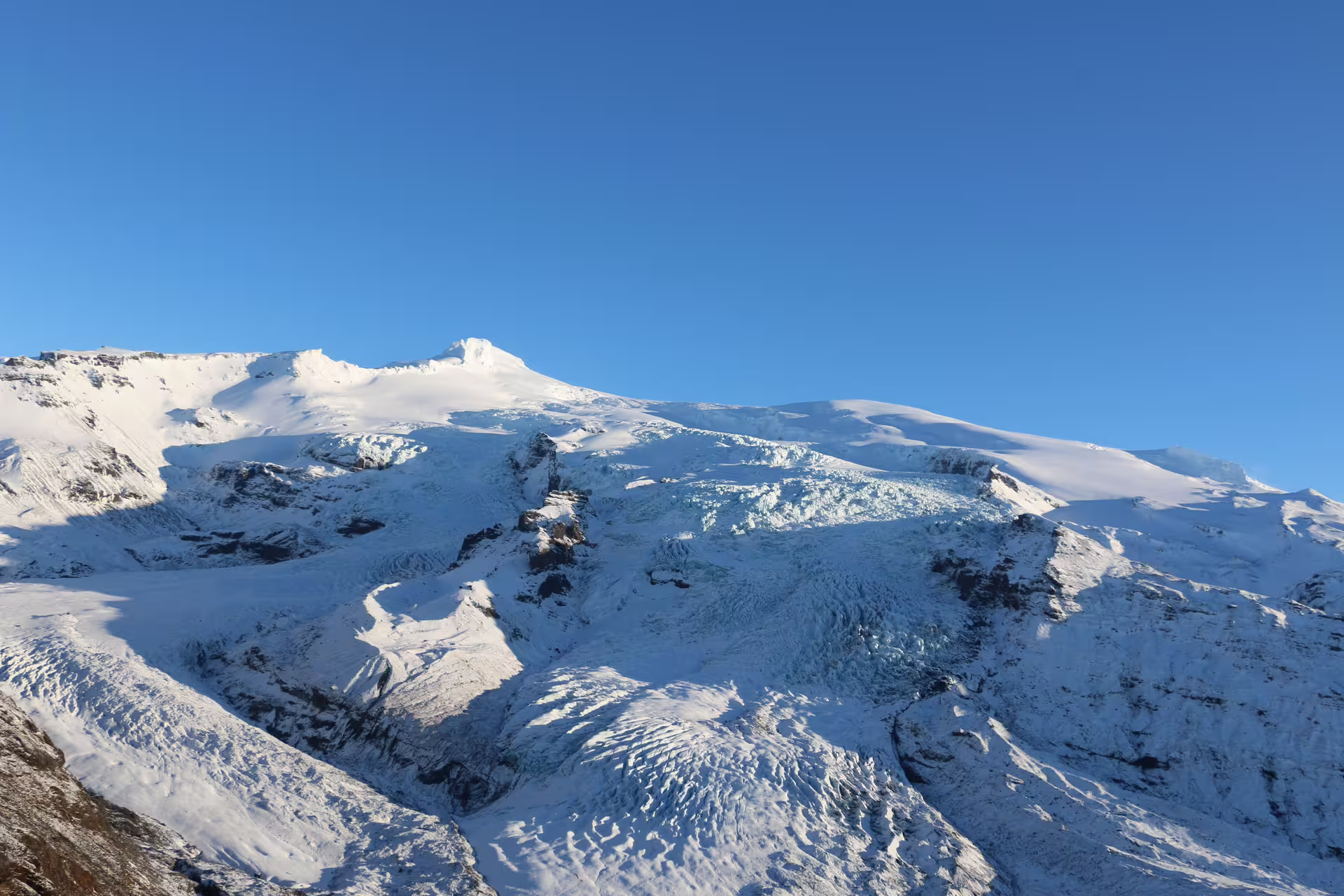 Aerial view of Vatnajokull glacier with icefall and snow-covered peaks under clear blue sky, Iceland