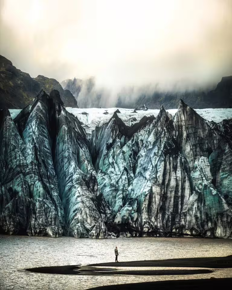 A lone traveler stands before towering jagged glacier formations on Iceland's South Coast, showcasing the awe-inspiring scale of Vatnajokull glacier on a private tour.