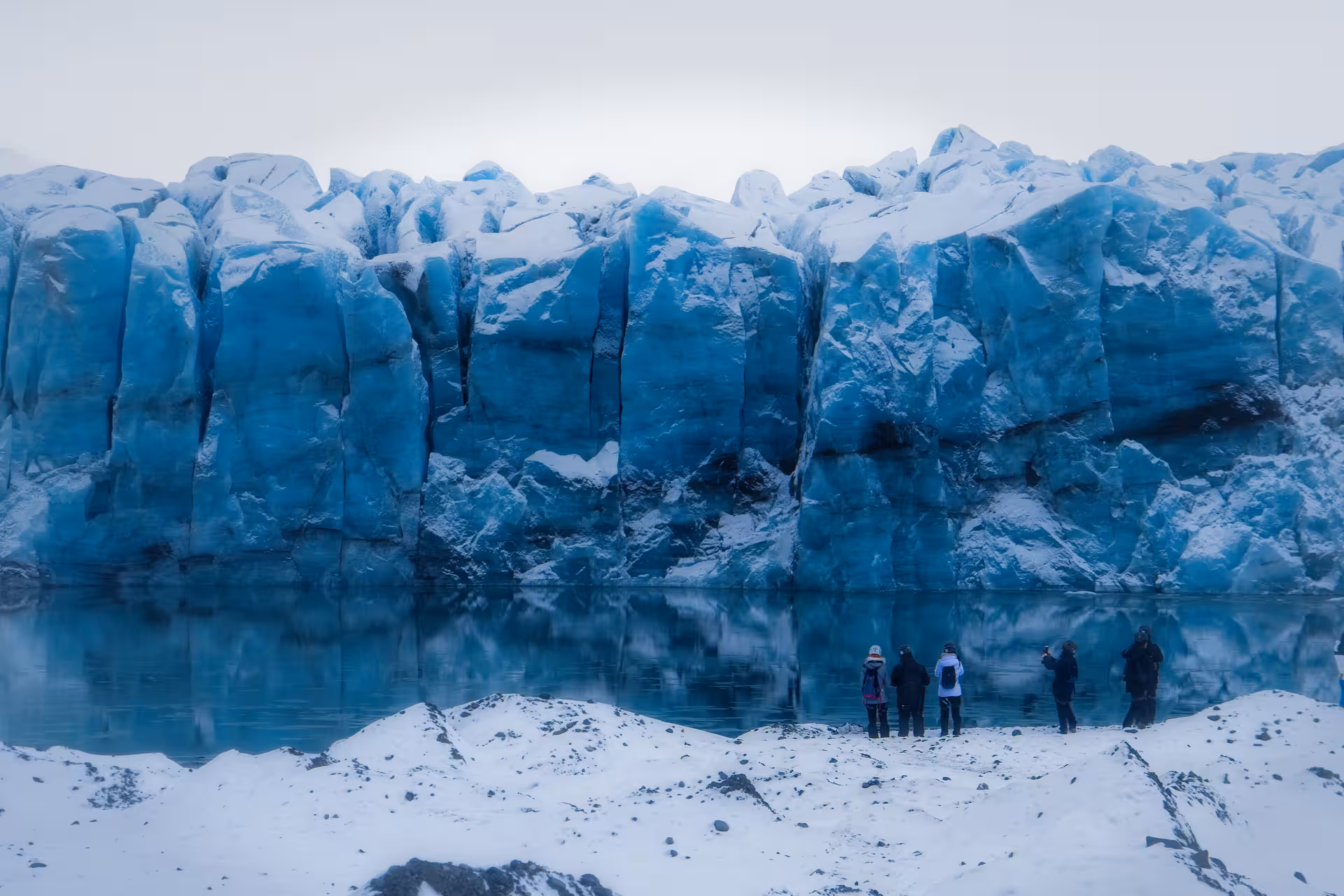 Tourists standing before the towering blue ice wall of Vatnajokull glacier near Jokulsarlon lagoon