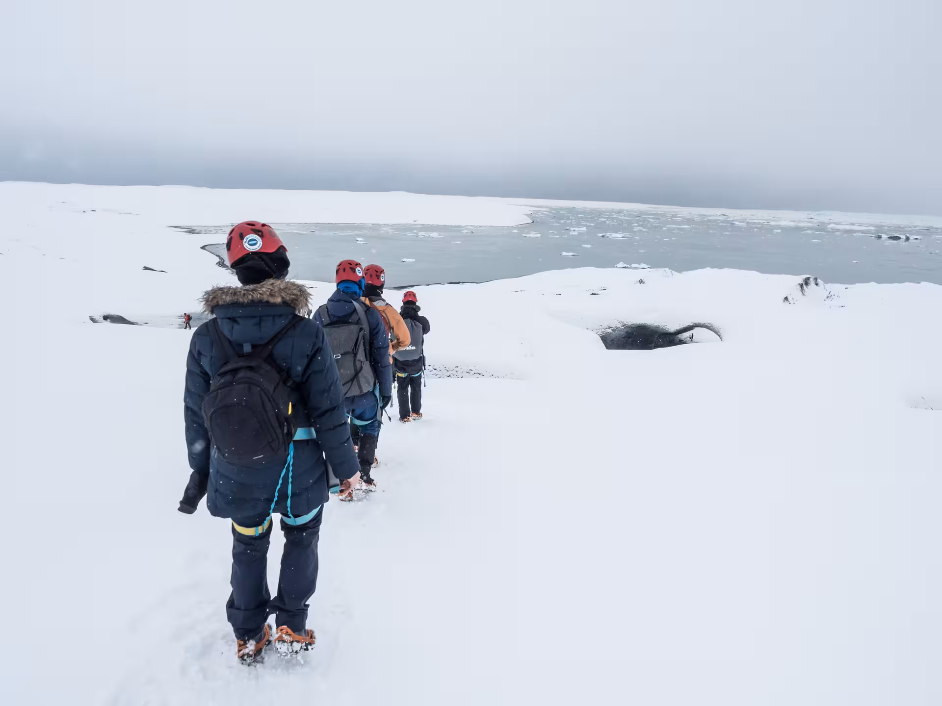 Tourists in red helmets and crampons snowshoeing across Vatnajokull glacier near Jokulsarlon lagoon