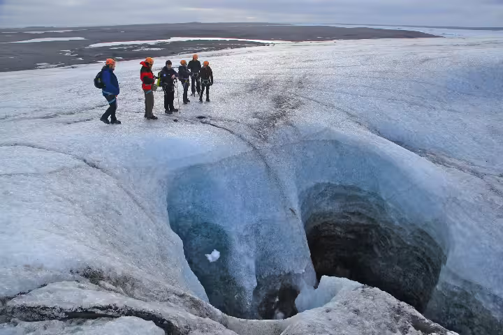 Group of hikers in safety gear exploring a moulin on Vatnajokull glacier, Iceland