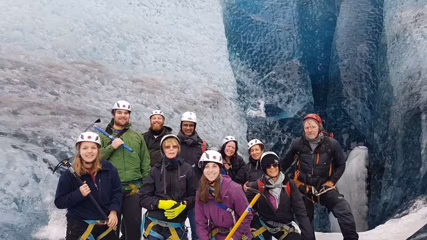 Group of tourists with helmets and ice axes posing inside Vatnajokull glacier crevasse during guided glacier walk