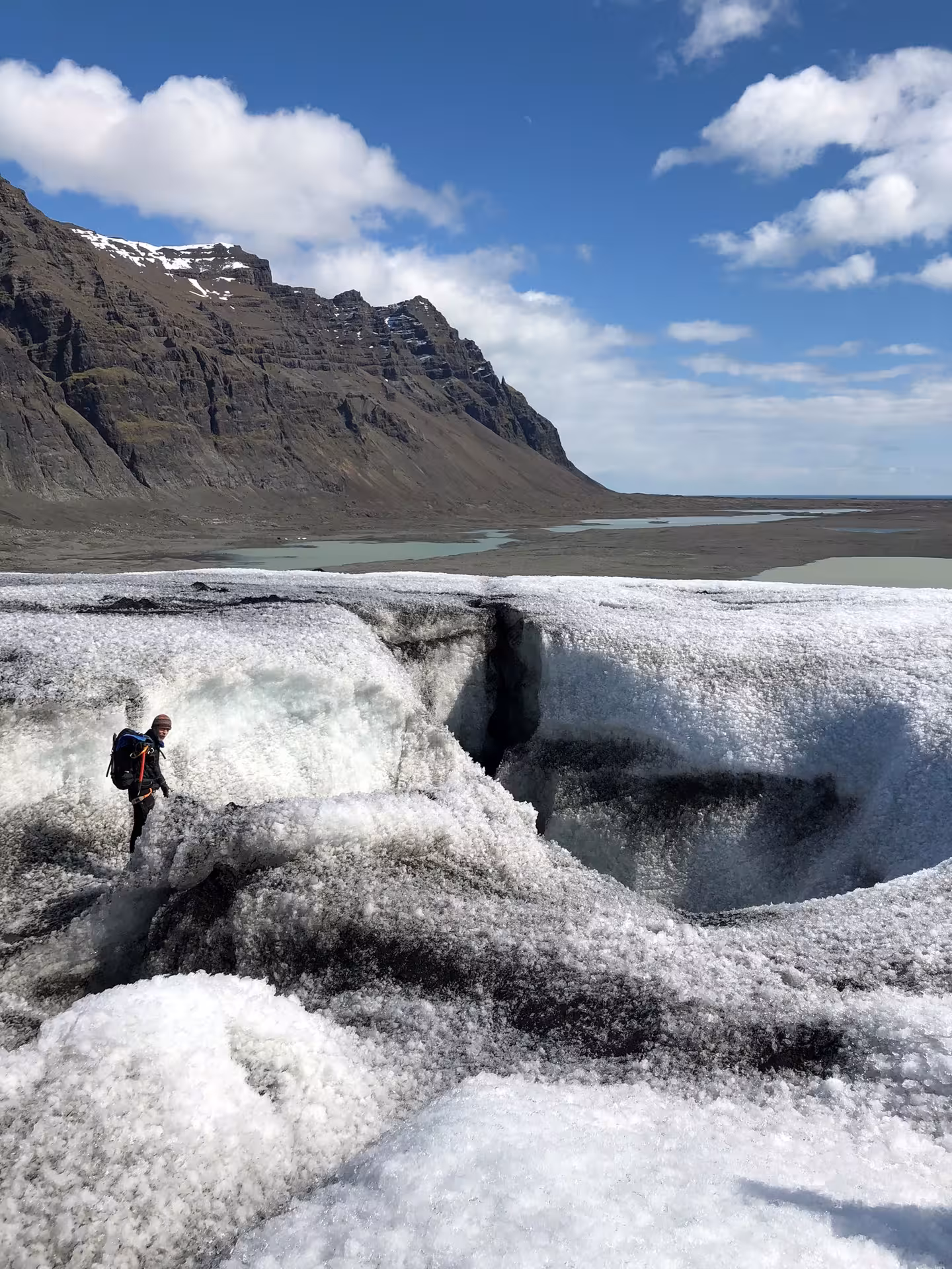 Hiker with backpack standing on Vatnajokull glacier next to deep crevasse with mountain backdrop Iceland