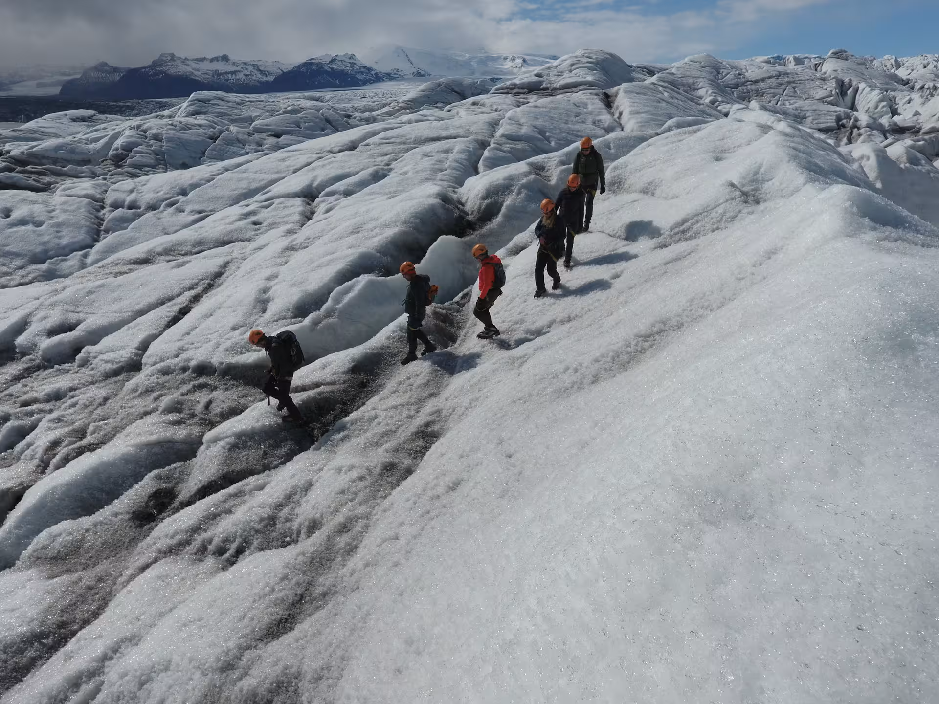 Group of hikers with orange helmets climbing Vatnajokull glacier in Iceland on a sunny day