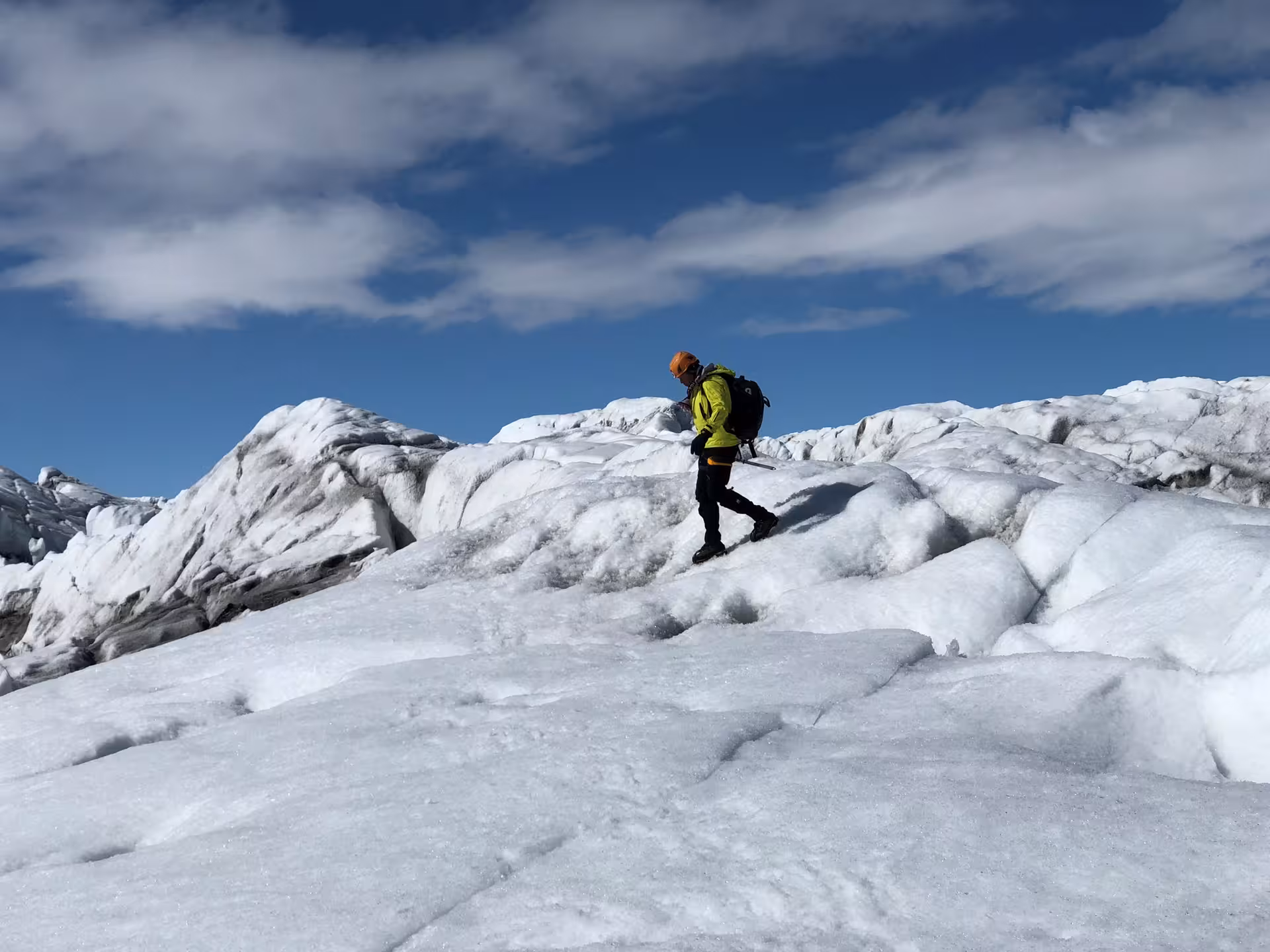Guide in yellow jacket and orange helmet ice climbing on Vatnajokull glacier under blue sky