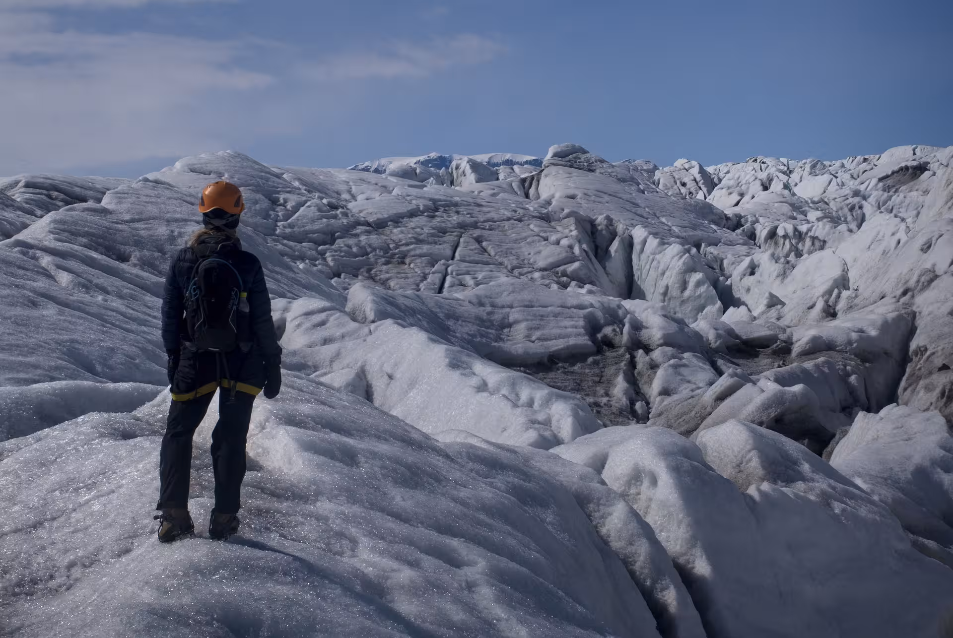 Hiker with orange helmet and backpack standing on Vatnajokull glacier surveying icy terrain in Iceland