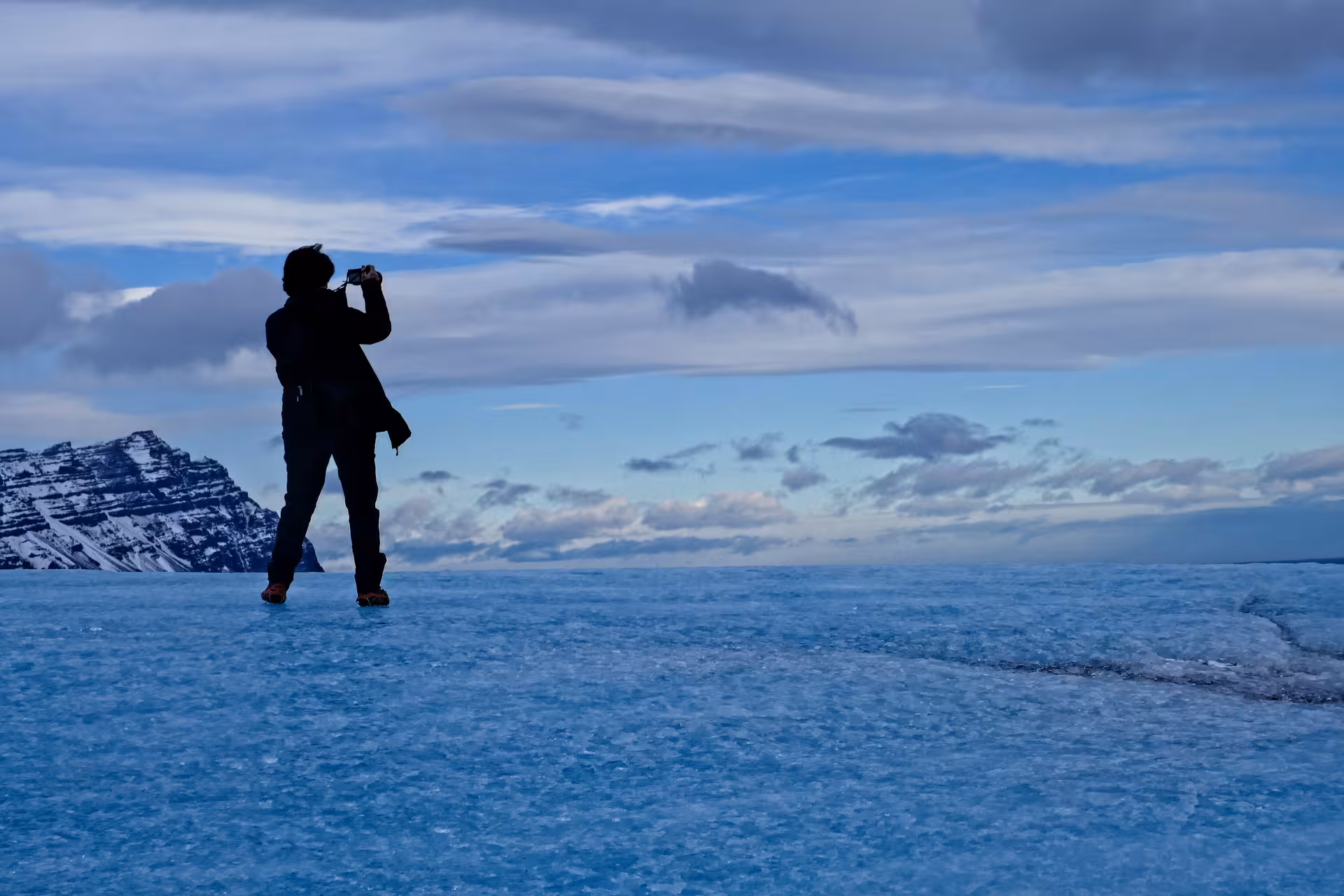 Silhouette of a person photographing the vast blue Vatnajokull glacier with snow-capped mountains in the background