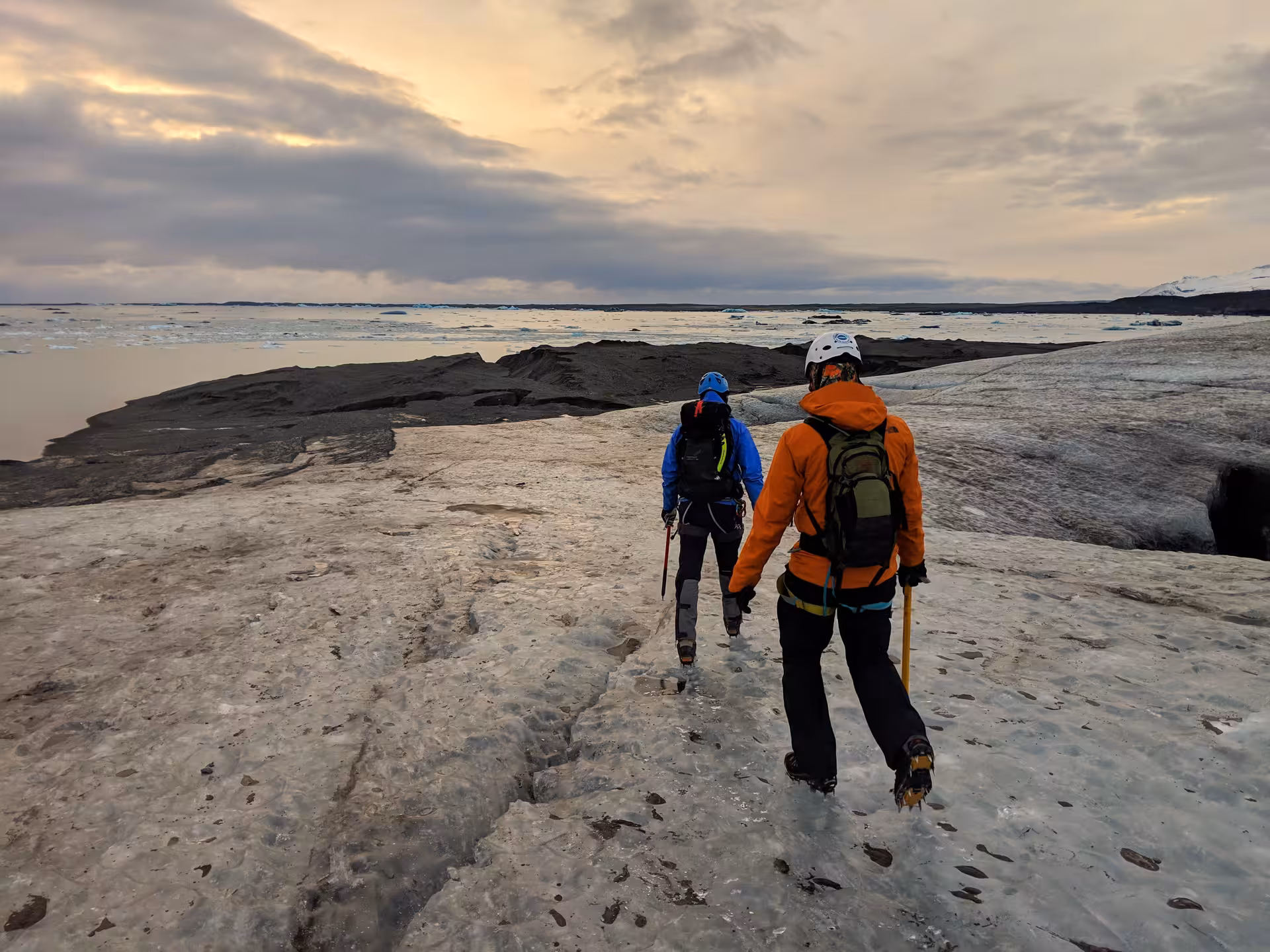 Two hikers with crampons and ice axes walking on Vatnajokull glacier toward Jokulsarlon iceberg lagoon