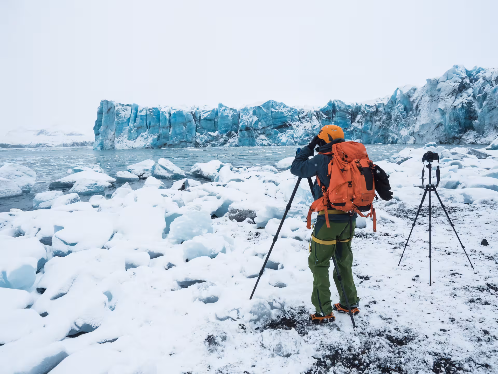 Photographer with orange backpack and crampons shooting glacier lagoon at Vatnajokull Iceland in winter