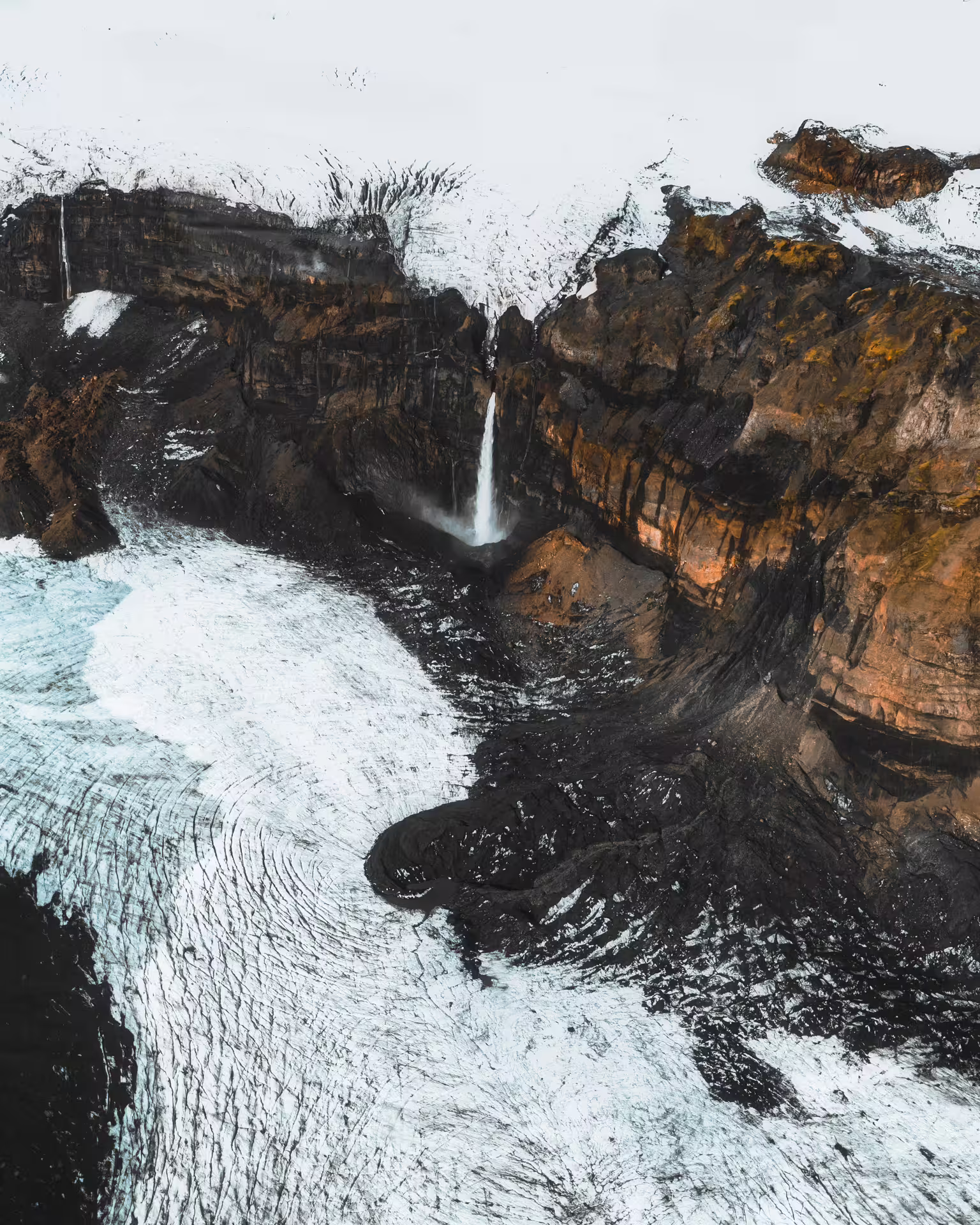Aerial view of Vatnajokull glacier with waterfall flowing into black volcanic rock canyon, Iceland