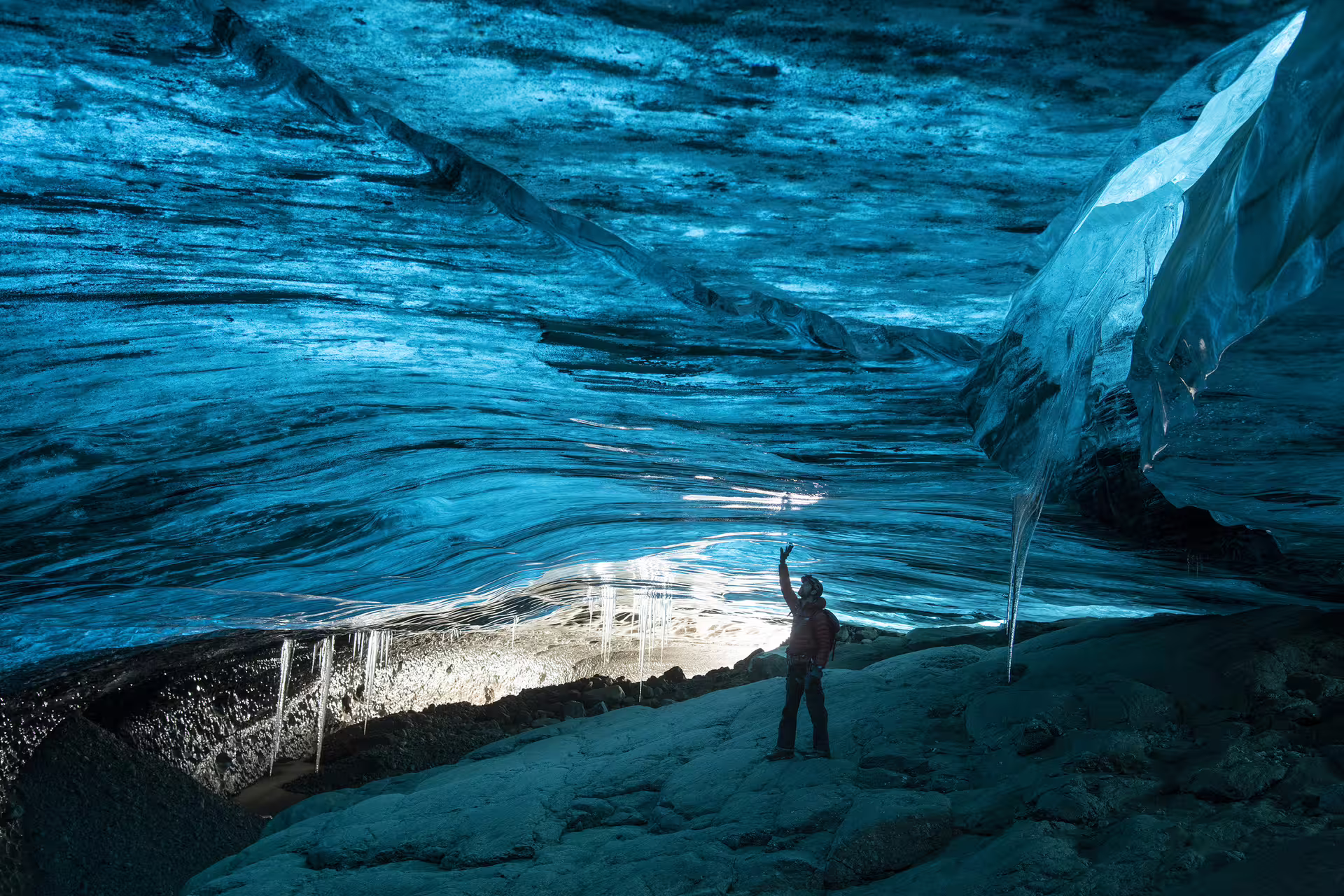Explorer reaching toward glowing blue ice ceiling inside Vatnajokull glacier ice cave Iceland