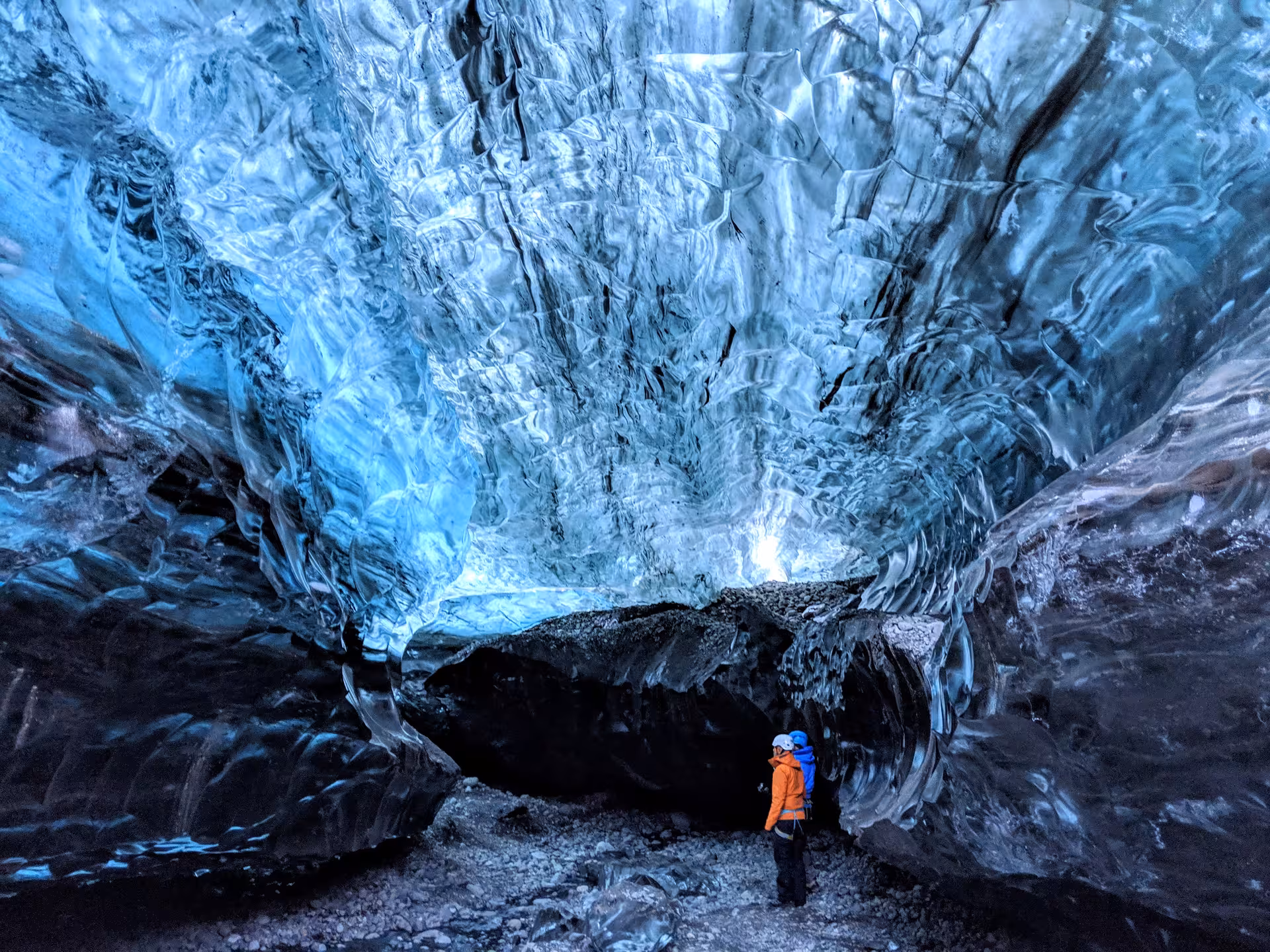 Two explorers in orange and blue jackets standing inside a stunning blue Vatnajokull glacier ice cave in Iceland