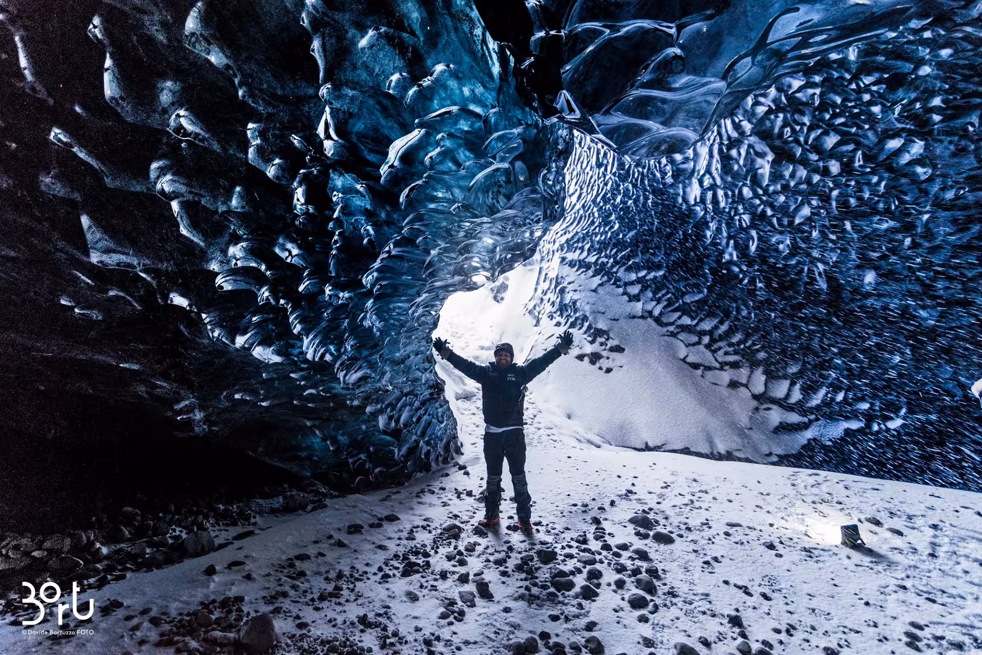 Person with arms raised inside Vatnajokull glacier ice cave with blue ice formations in Iceland