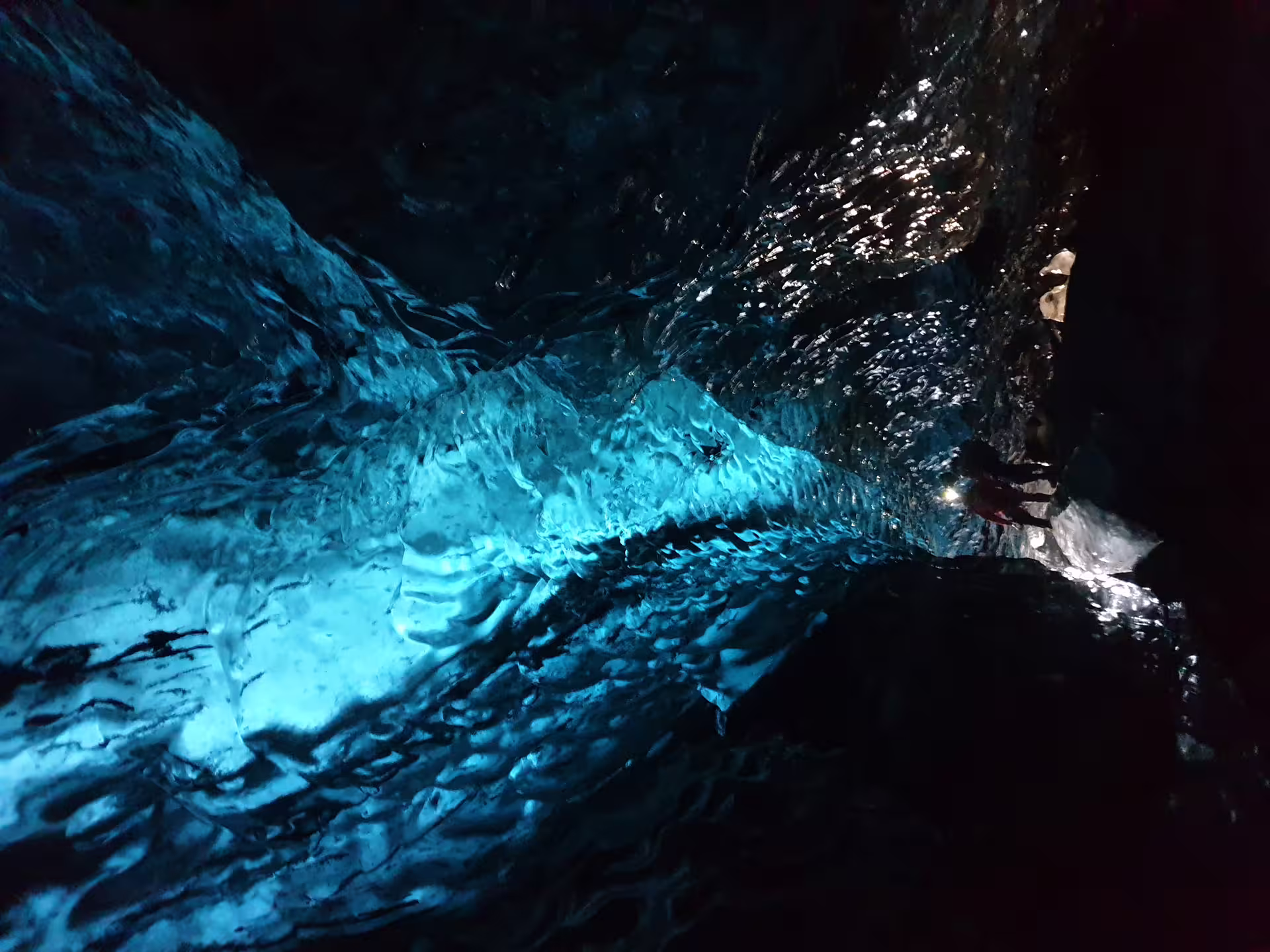 Glowing blue ice cave interior at Vatnajokull glacier with visitors exploring the tunnel