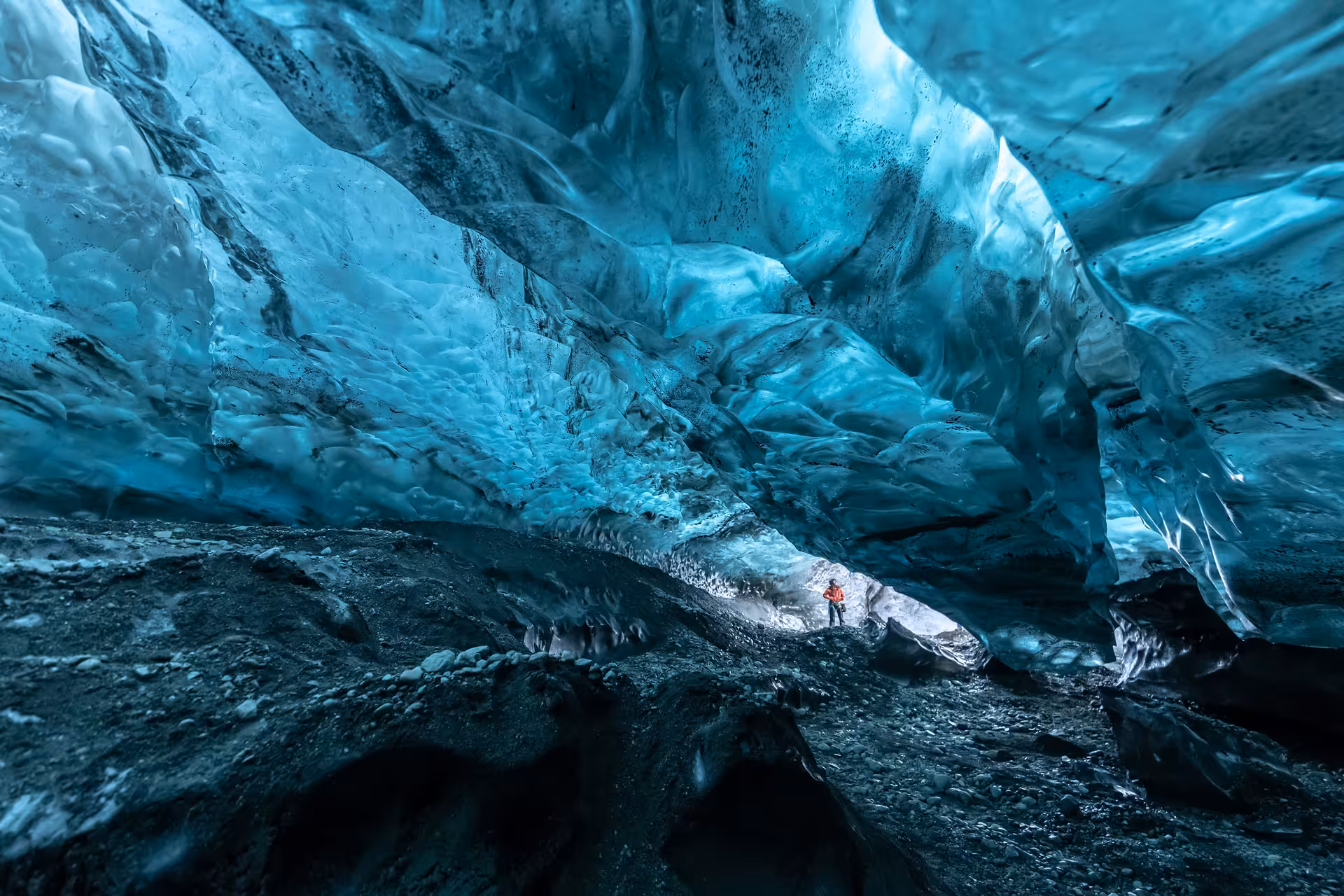 Explorer in red jacket inside Vatnajokull glacier ice cave with glowing blue ice walls