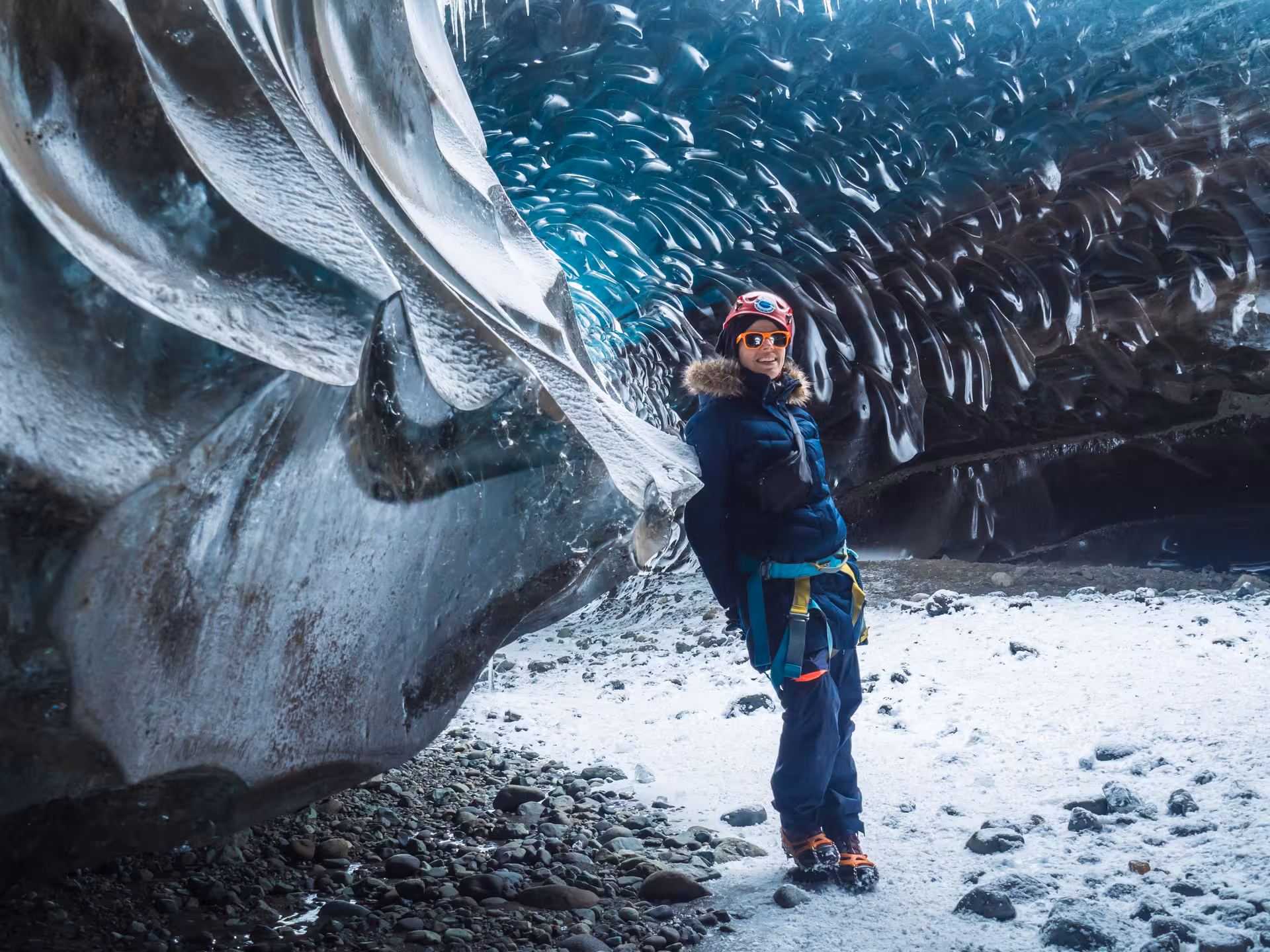 Explorer in blue gear standing inside Vatnajokull glacier ice cave with textured blue ice walls