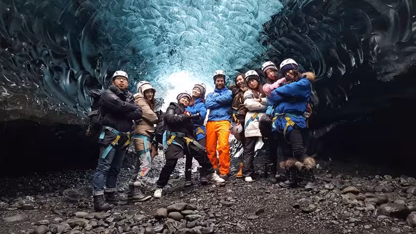 Tour group in helmets and harnesses posing inside Vatnajokull glacier ice cave Iceland